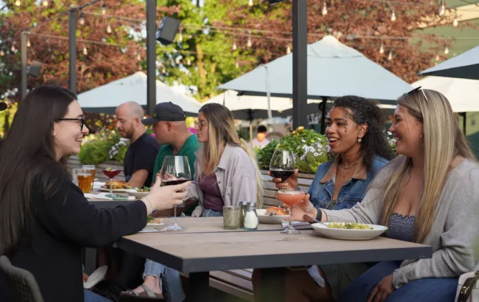 Group of friends dining together with food and drinks on a lively outdoor restaurant patio.