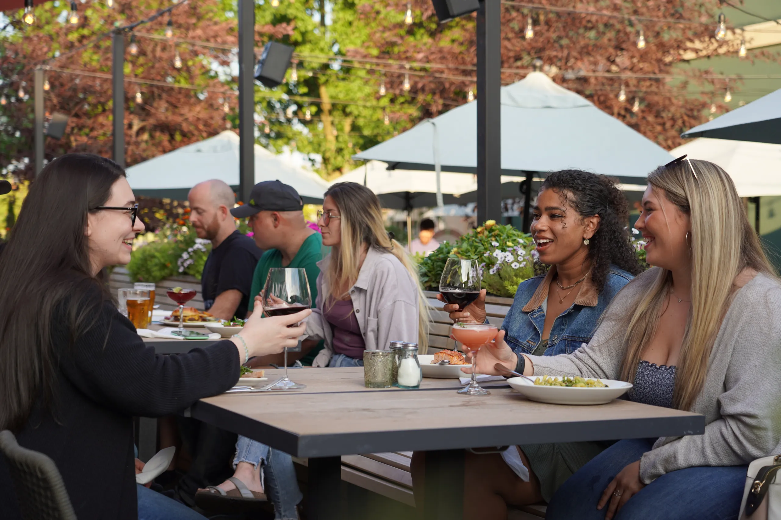 Group of friends dining together with food and drinks on a lively outdoor restaurant patio.